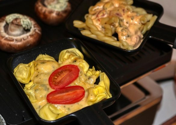 Petites poêlons de Raclette remplies de tortellinis gratinés et de pâtes, prêtes à être dégustées.
