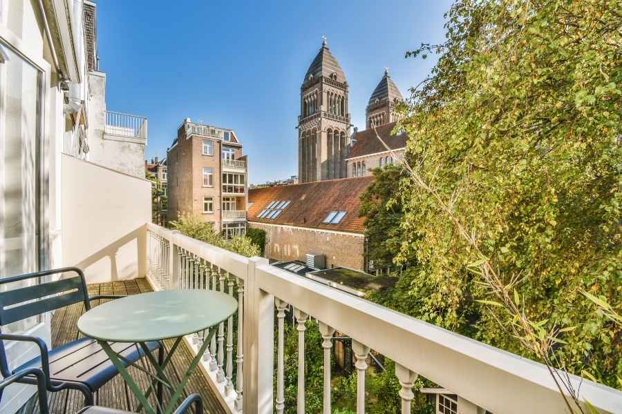 Un petit balcon étroit aménagé avec une table ronde et deux chaises métalliques offrant une vue urbaine.