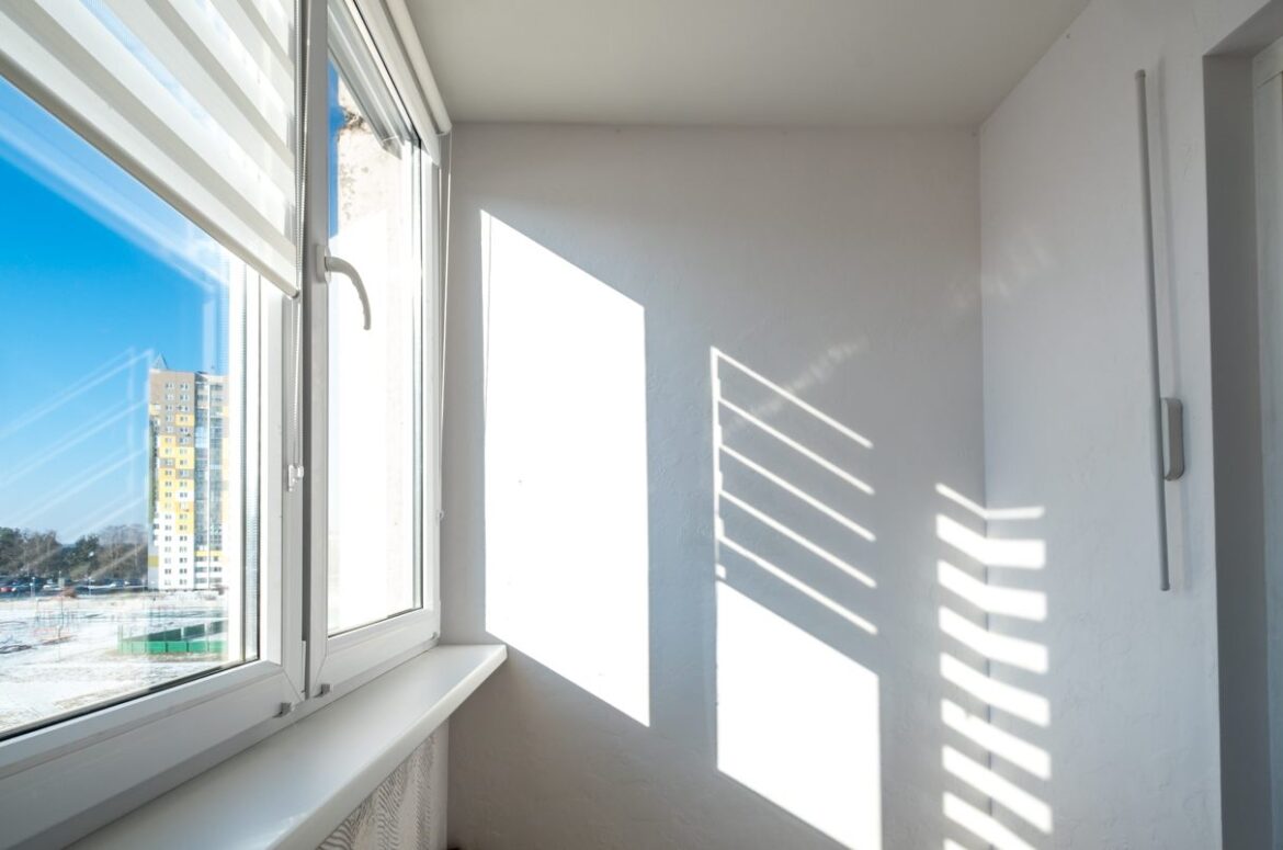 Fenêtre moderne en PVC blanc avec stores partiellement ouverts, laissant passer la lumière du soleil sur un mur blanc, témoignant de la duree de vie moyenne menuiserie pvc.